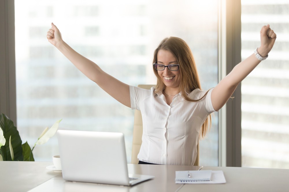 a woman celebrating in front of a laptop