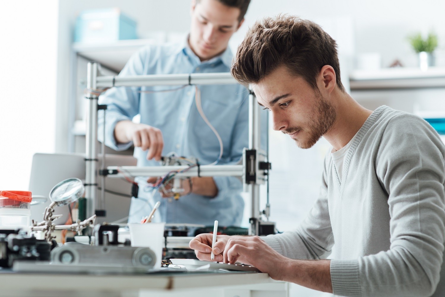 Man works on 3D printer while another works on a tablet