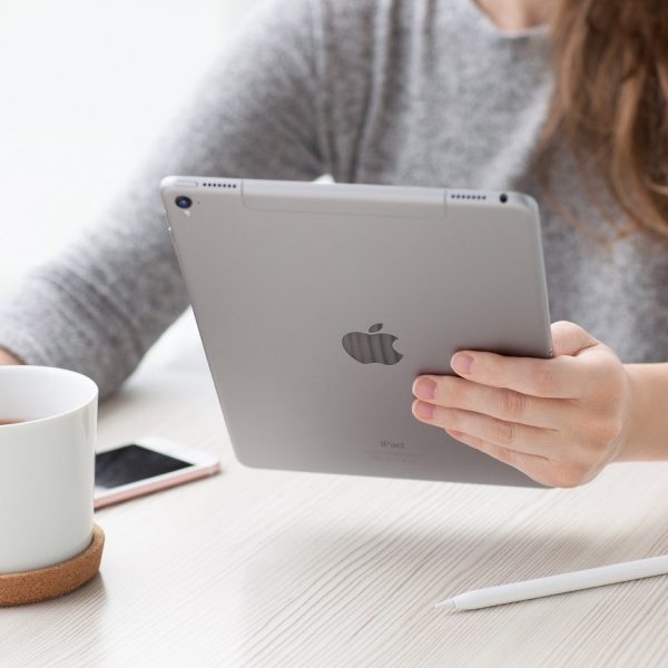 A woman with an iPad in one hand and a cup of coffee in the other