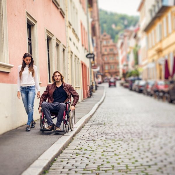 A man in wheelchair on sidewalk with a woman walking beside him