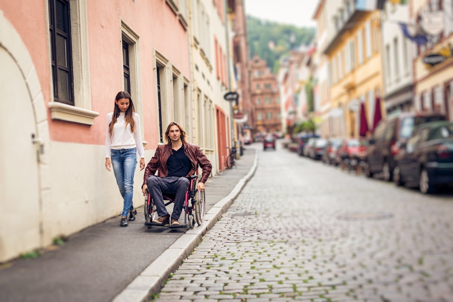A man in wheelchair on sidewalk with a woman walking beside him