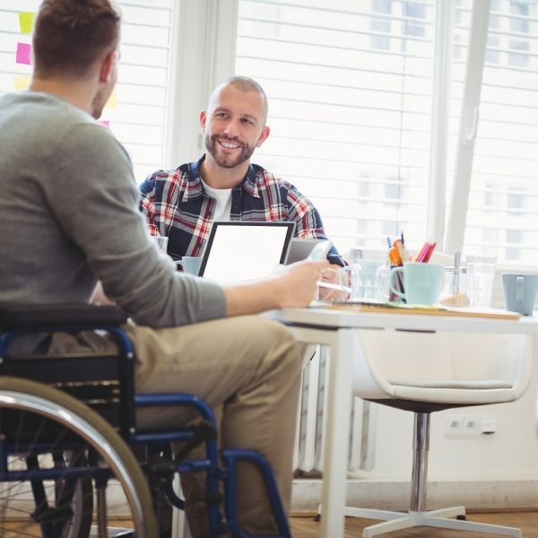 A man in a wheelchair in an office setting in conversation with another man at a desk