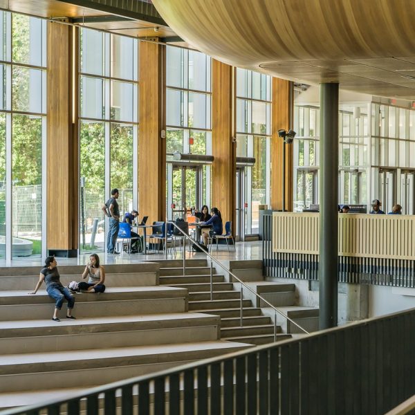 students sitting on stairs with large glass windows behind them