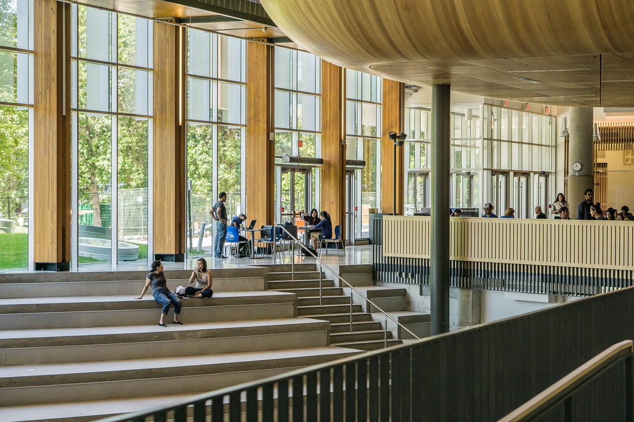 students sitting on stairs with large glass windows behind them