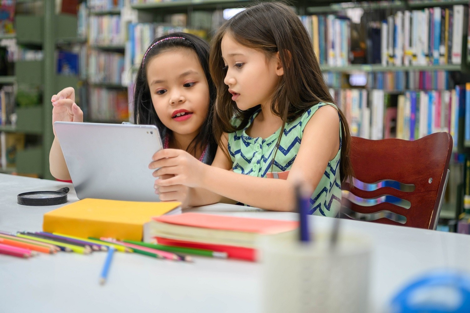 two children looking at an iPad in a library