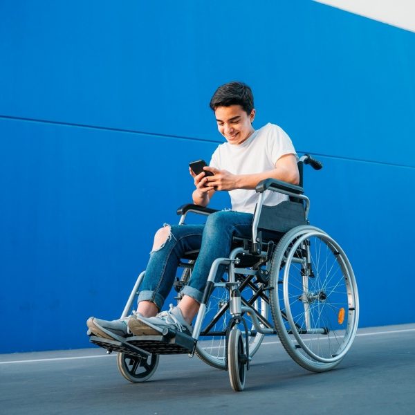 Youth seated in wheelchair, outdoors, using his phone and smiling