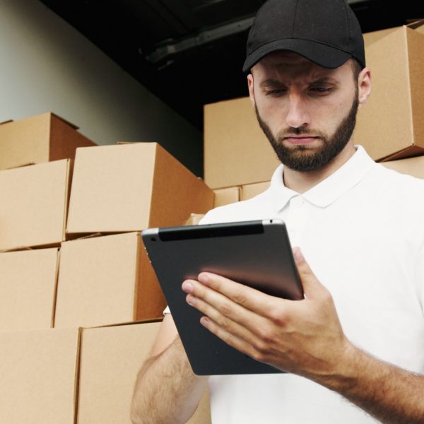 man using a tablet; piles of boxes behind him