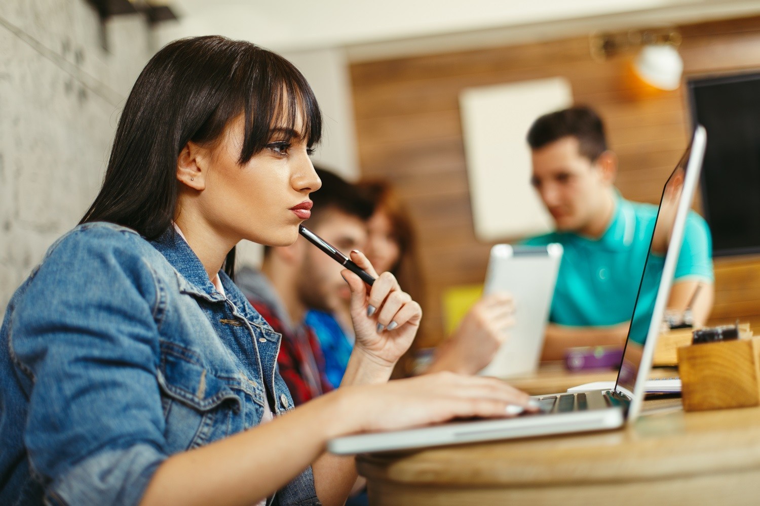 A classroom setting. In the foreground, a student is using a laptop