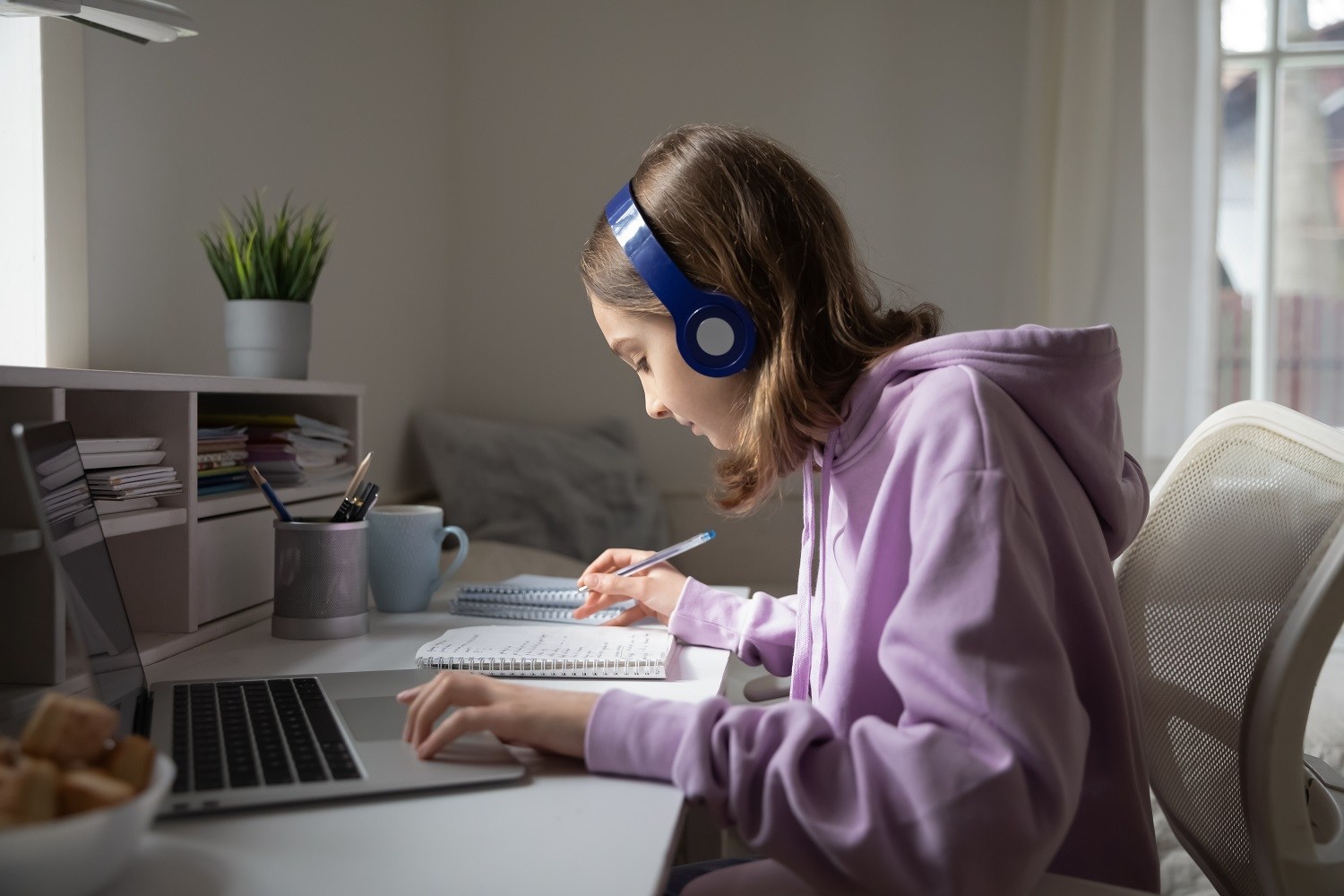 a student using headphones while working on her laptop and writing in a notebook