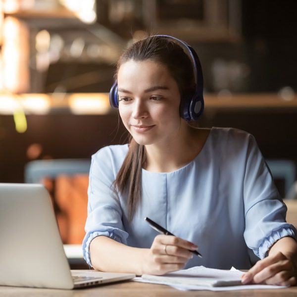 student using headphones while taking notes and looking at a laptop