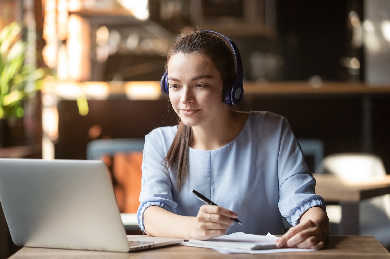 student using headphones while taking notes and looking at a laptop