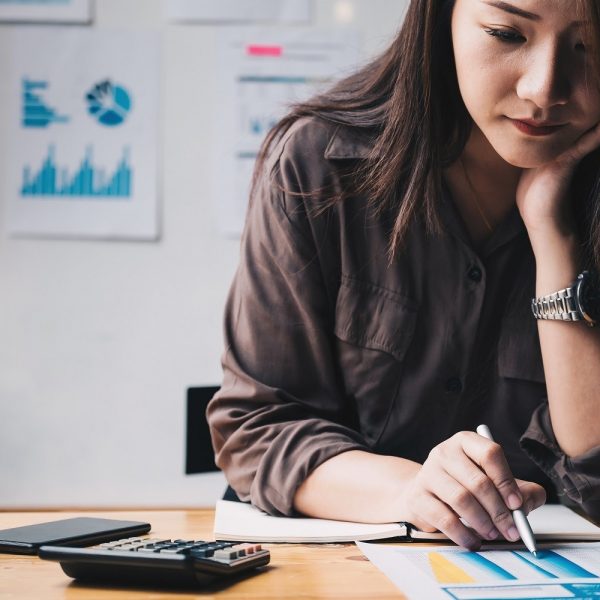 A student at a desk, making notes using a pen. A calculator is on the desk.