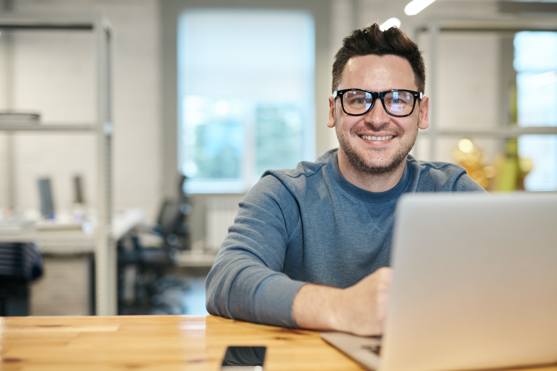 man seated at a desk with his laptop, smiling