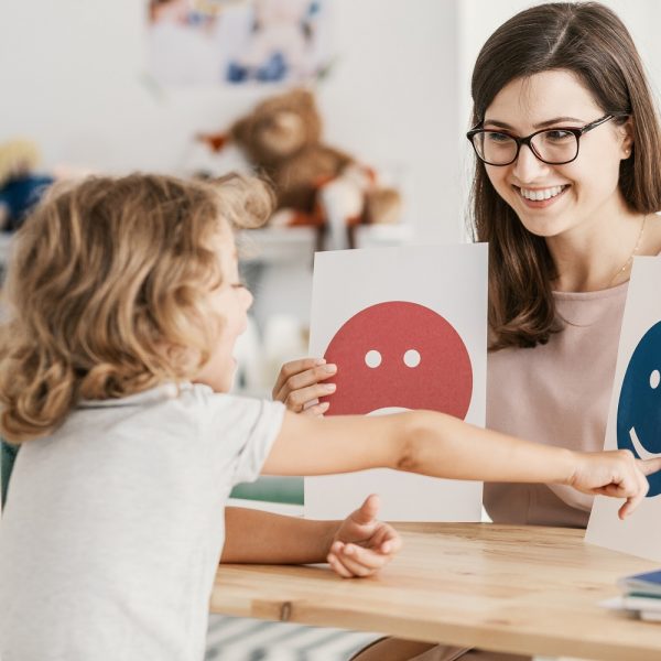 A woman holding up two signs, one with a happy emoji and one with a sad emoji. A child points at the happy face