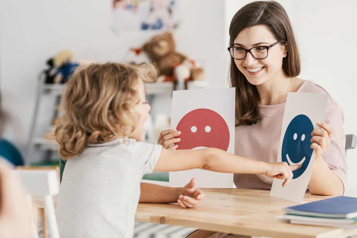 A woman holding up two signs, one with a happy emoji and one with a sad emoji. A child points at the happy face