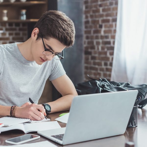 a student writing notes, with a laptop in front of him