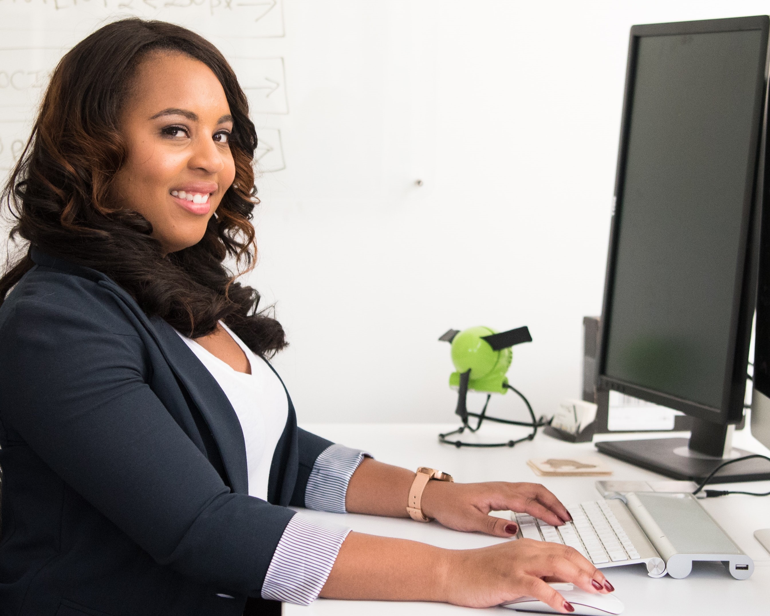 A woman working at a desk, using a keyboard and mouse. She is smiling at the camera