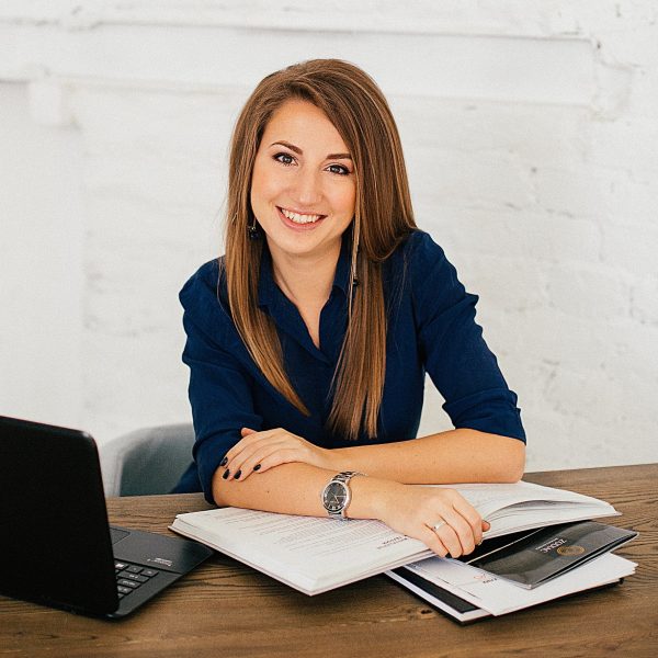 A woman seated at a desk. Papers in front of her and a laptop to the side.