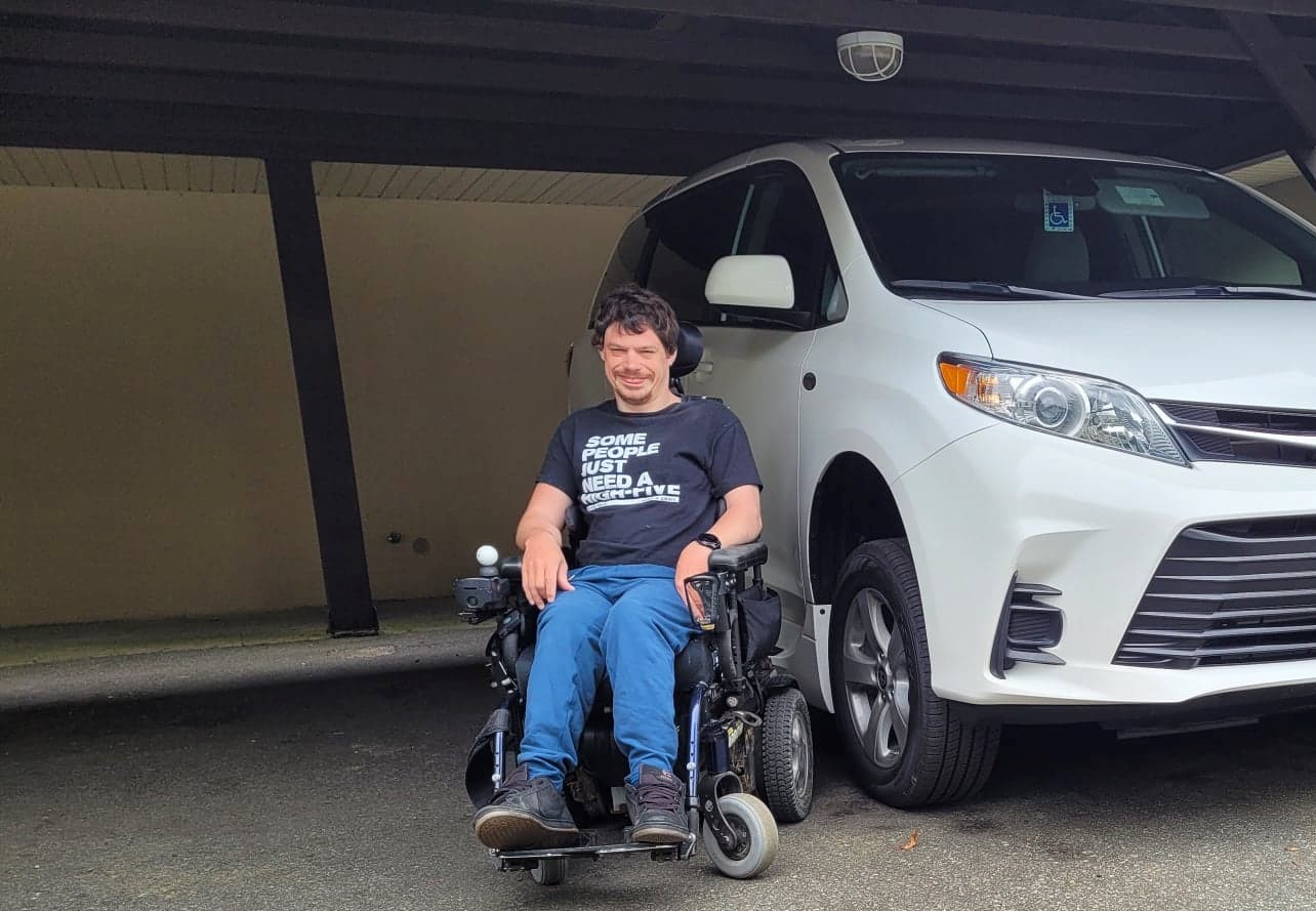 Shayne smiling in front of his modified minivan