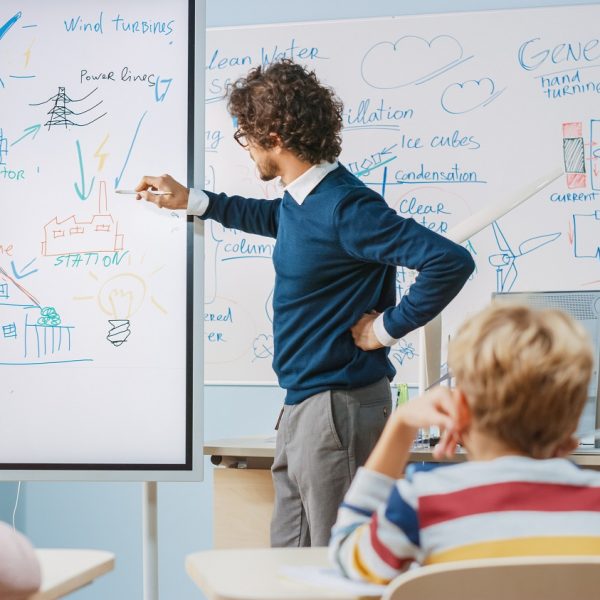 A teacher sketching a process for wind energy generation, with a group of students seated and watching