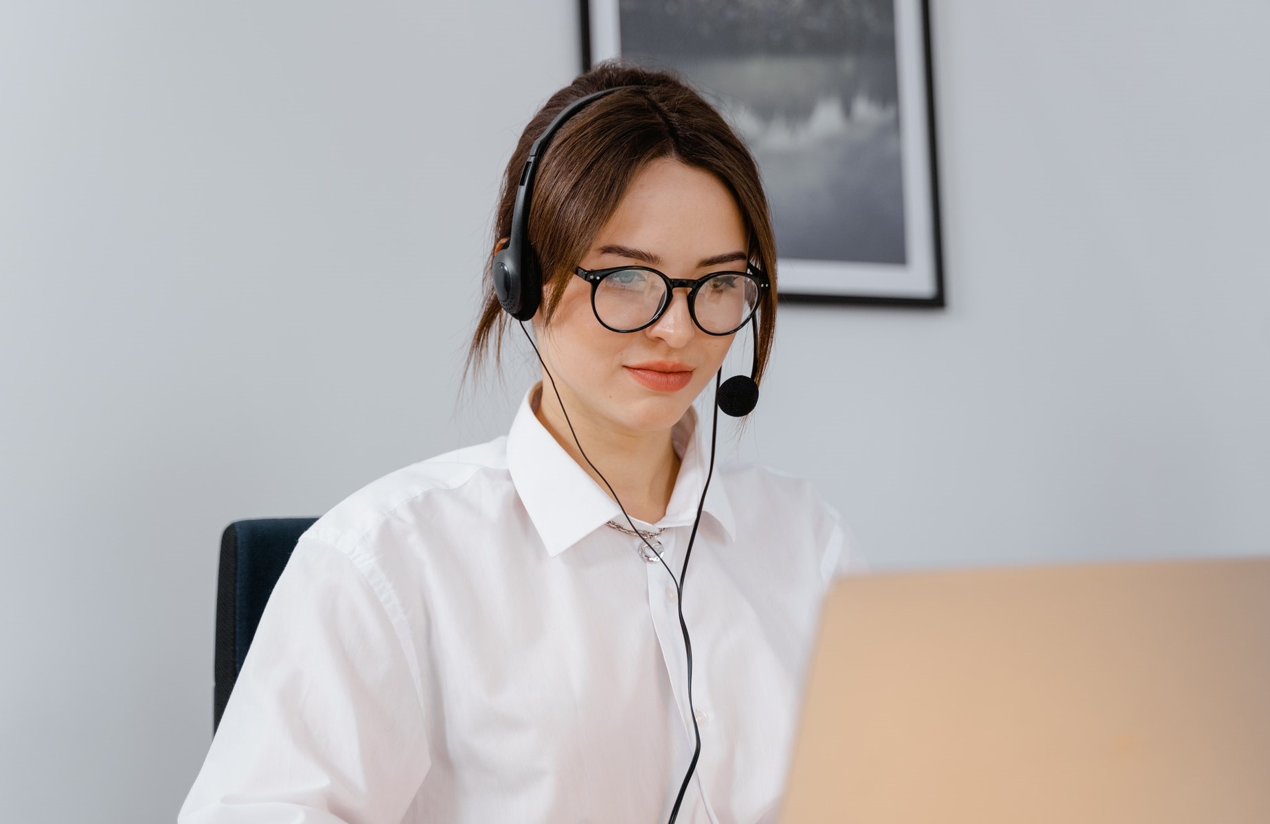 Woman seated at a desk, using headphones while looking at a laptop