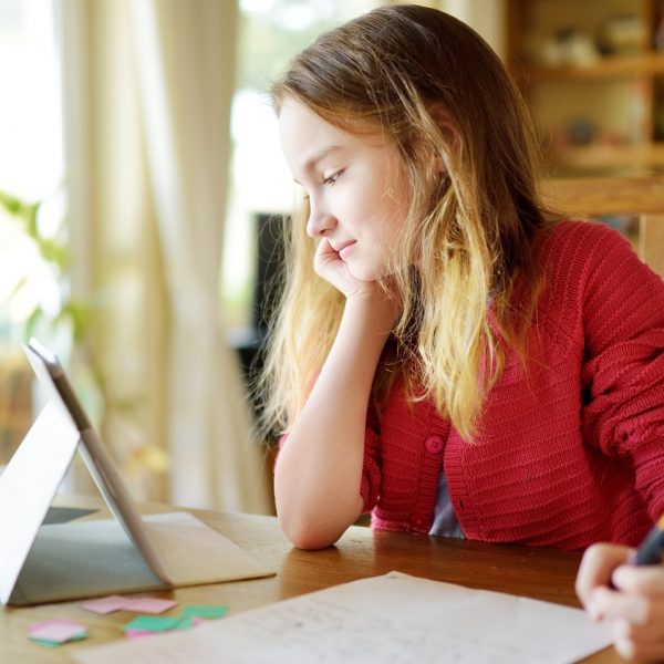 a girl looks at a tablet while doing homework