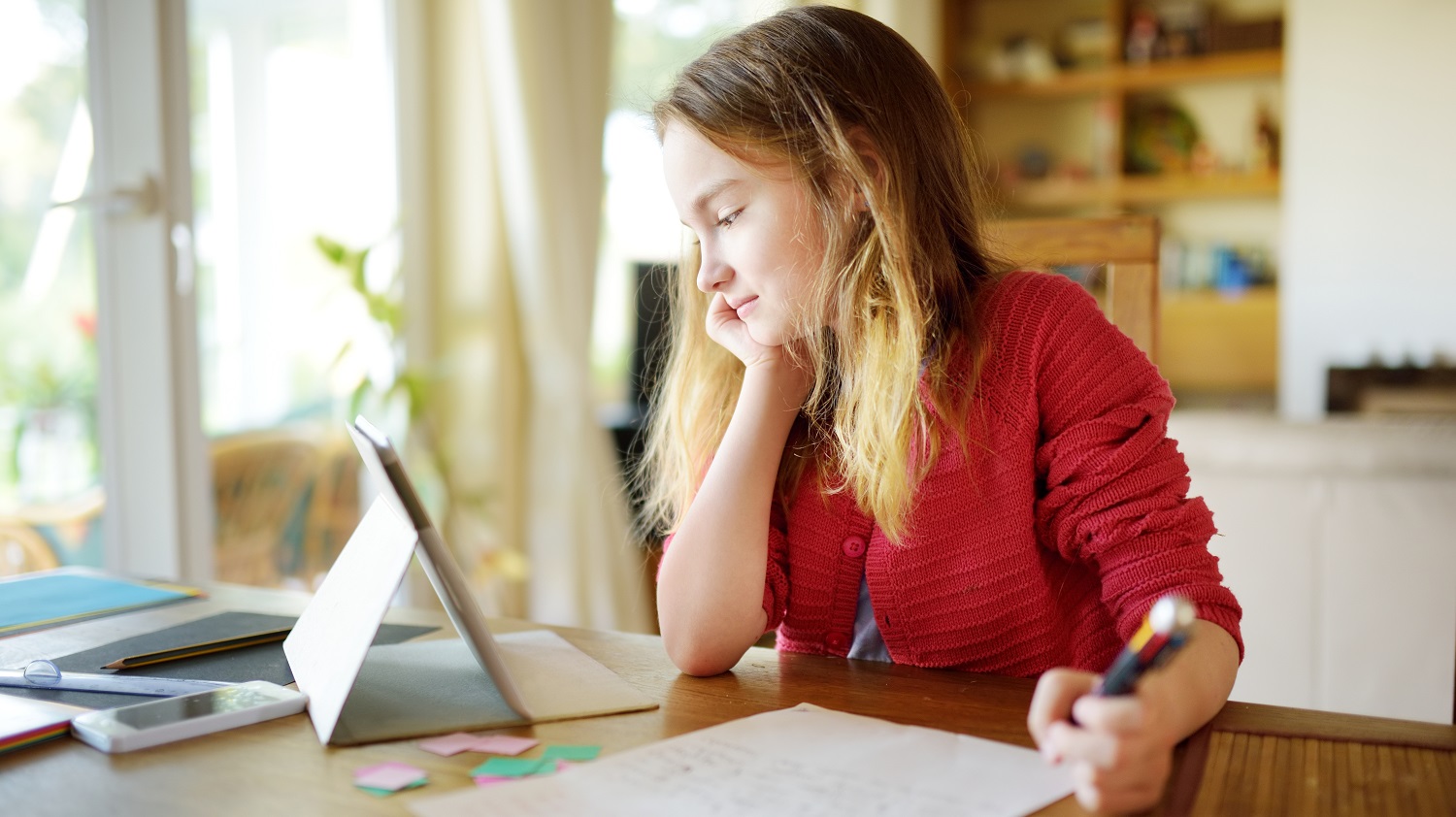 a girl looks at a tablet while doing homework