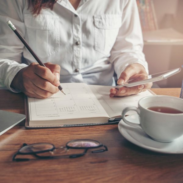 a person writing in a notebook, while checking on their phone