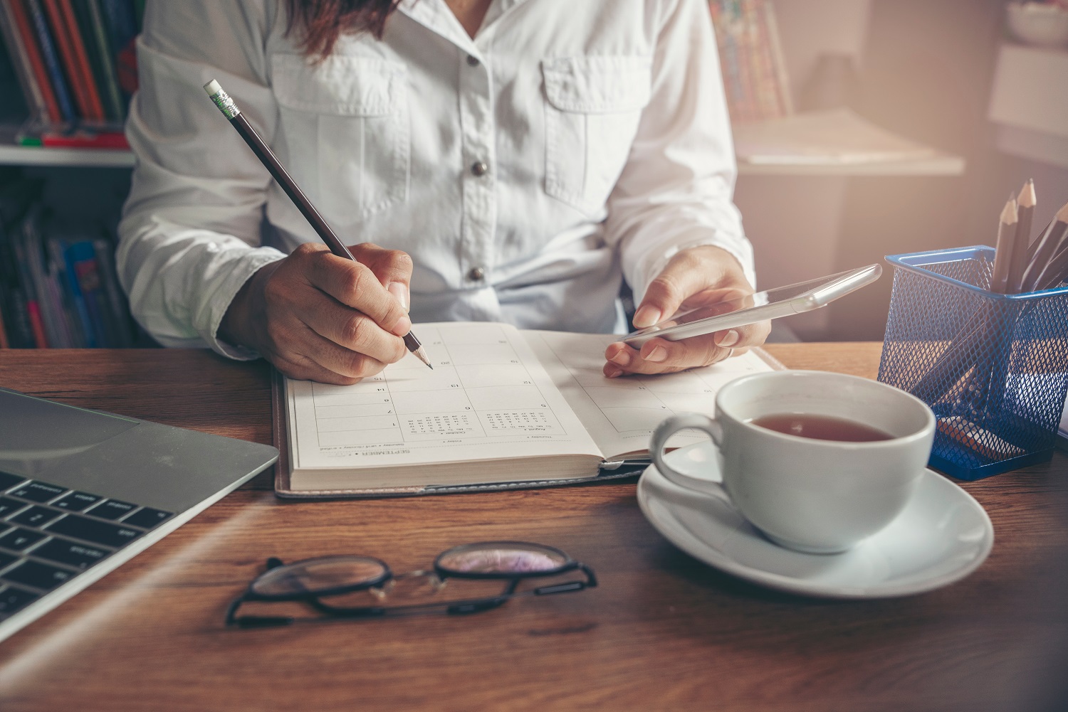 a person writing in a notebook, while checking on their phone