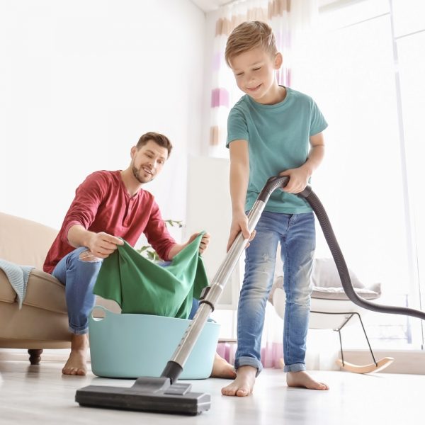 a father does laundry while his son vacuums