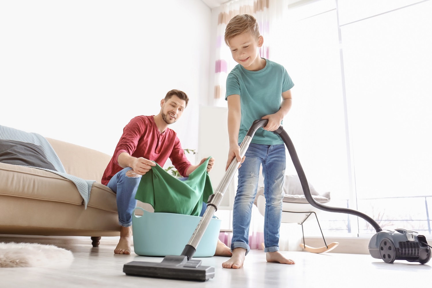 a father does laundry while his son vacuums