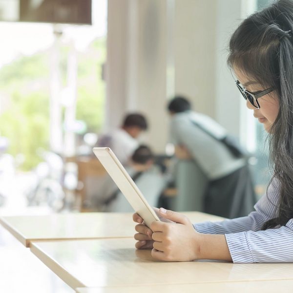 a girl with glasses reads on a tablet in a classroom