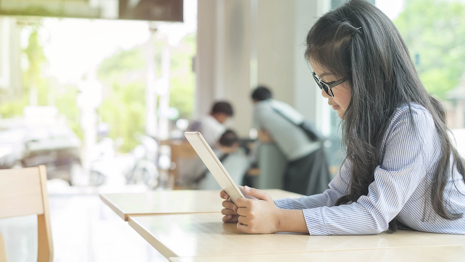 a girl with glasses reads on a tablet in a classroom