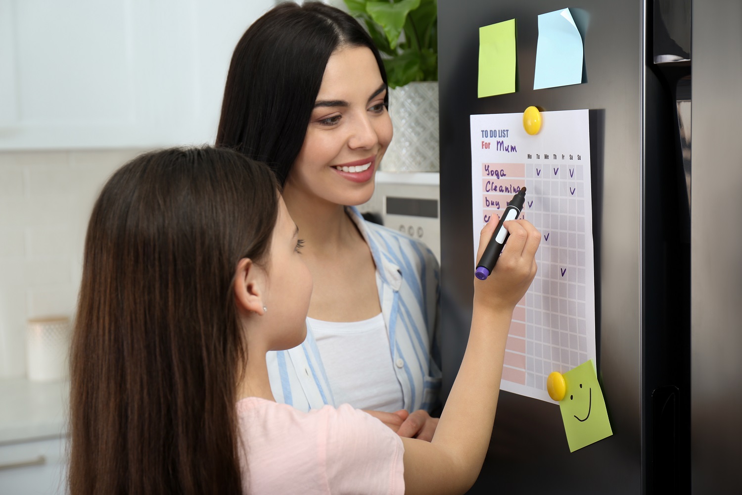 a mother watches as a little girl writes on a to-do list 