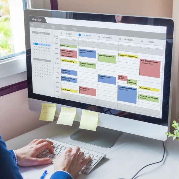 a person looks at an electronic calendar on a computer, and their computer has sticky notes with reminders attached