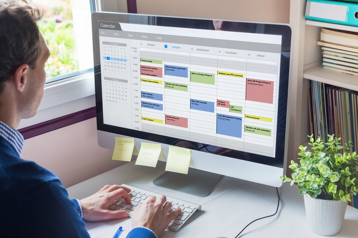 a person looks at an electronic calendar on a computer, and their computer has sticky notes with reminders attached