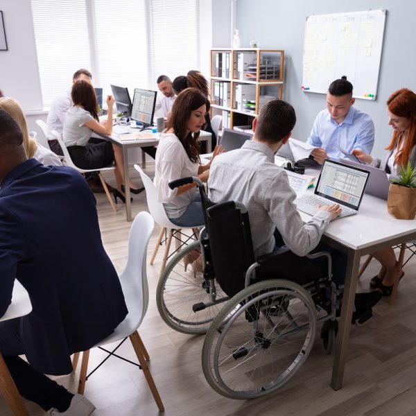 diverse groups of people working in an office, including a man in a wheelchair