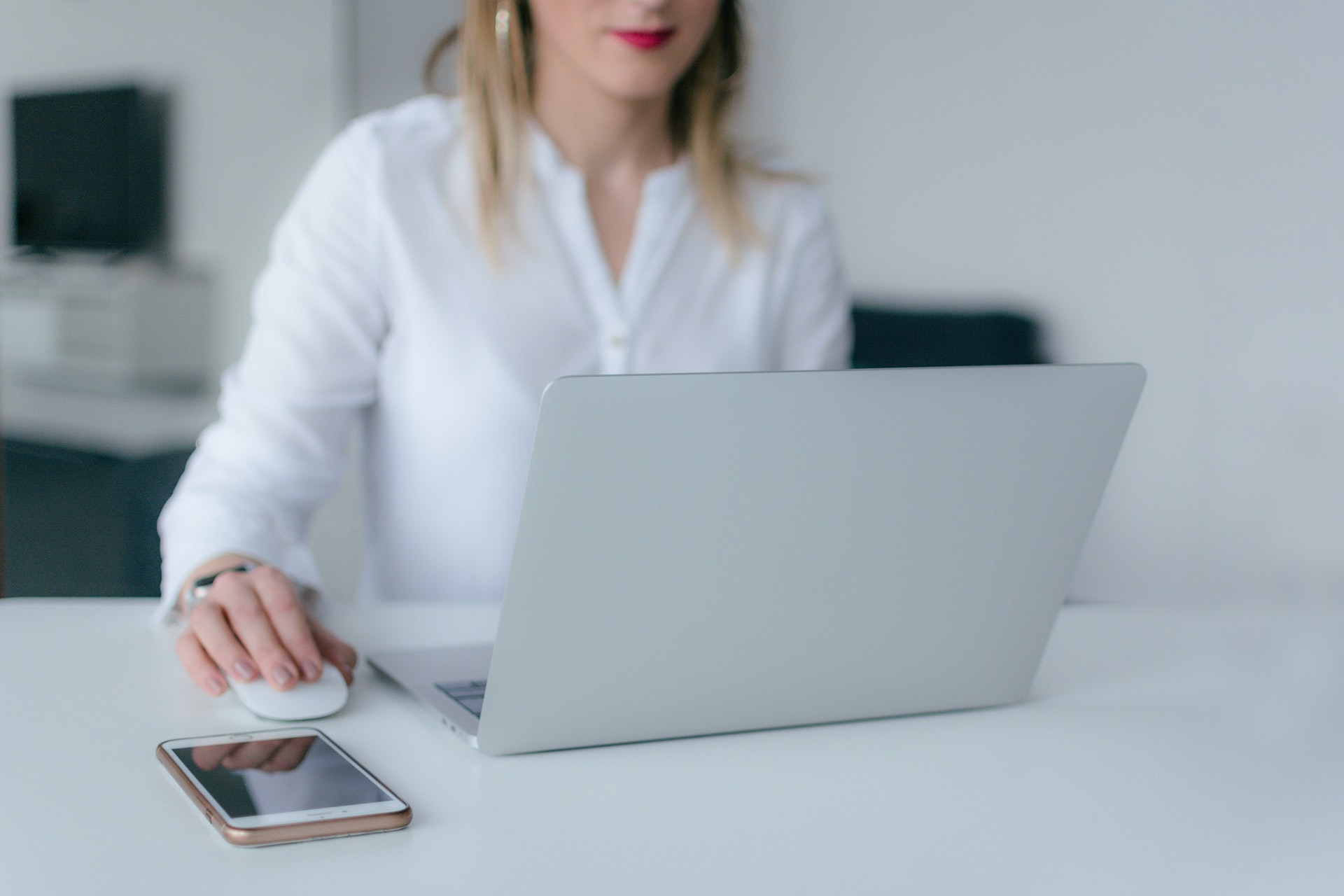 a woman uses her laptop, with her phone nearby on the table