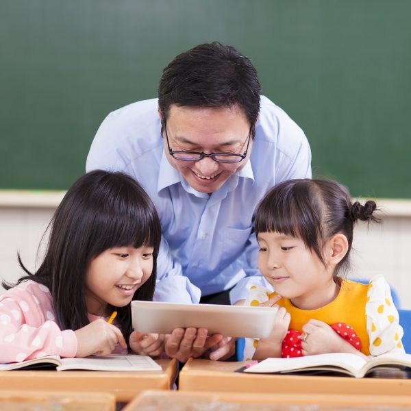a teacher showing two girls a video on a tablet in a classroom