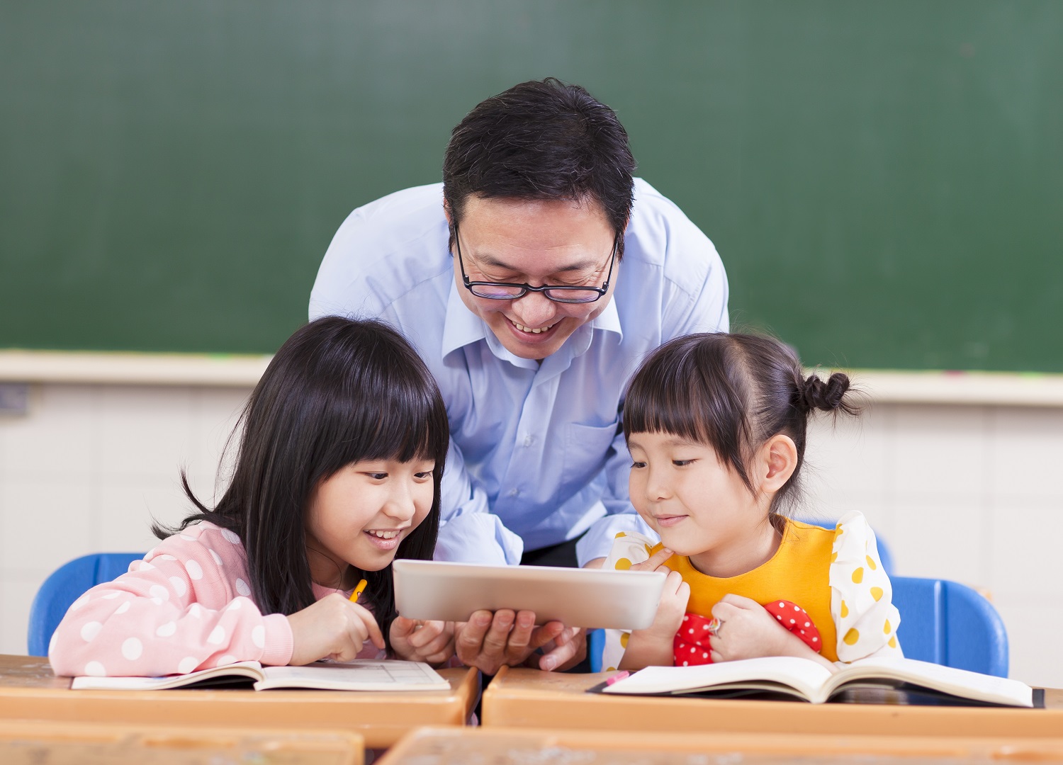 a teacher showing two girls a video on a tablet in a classroom