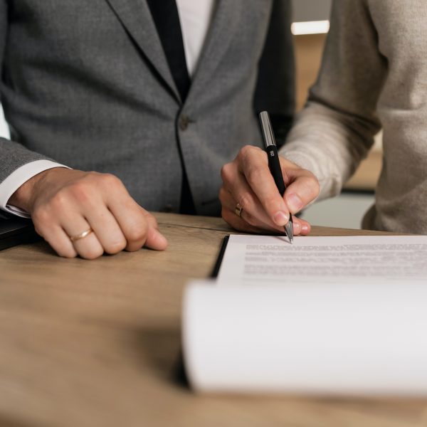 a person signs documents while a man in a suit watches