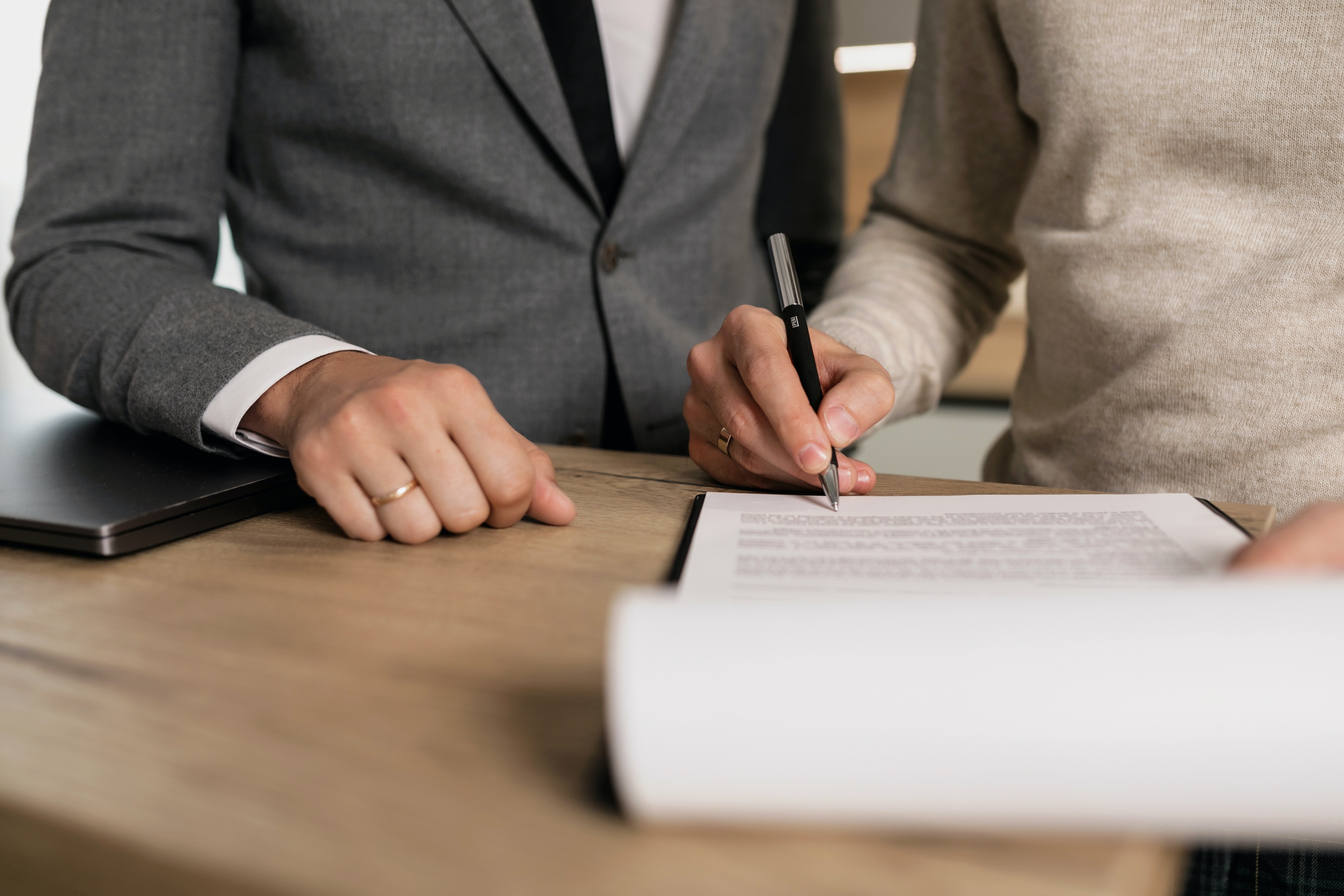 a person signs documents while a man in a suit watches