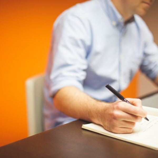 a man writing notes in a notepad while going on the laptop