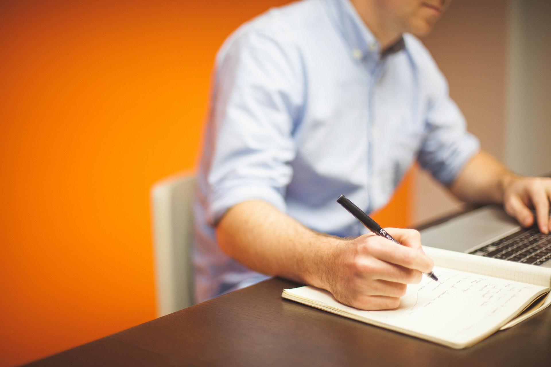 a man writing notes in a notepad while going on the laptop