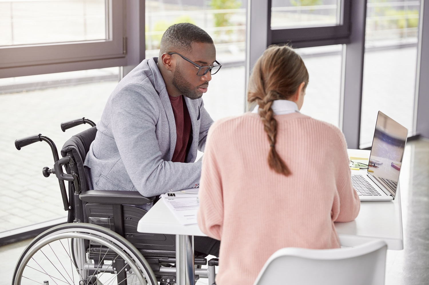 a woman works with a man in a wheelchair on a laptop