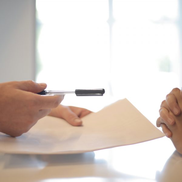 a person in a suit handing a customer a paper and pen to sign a document