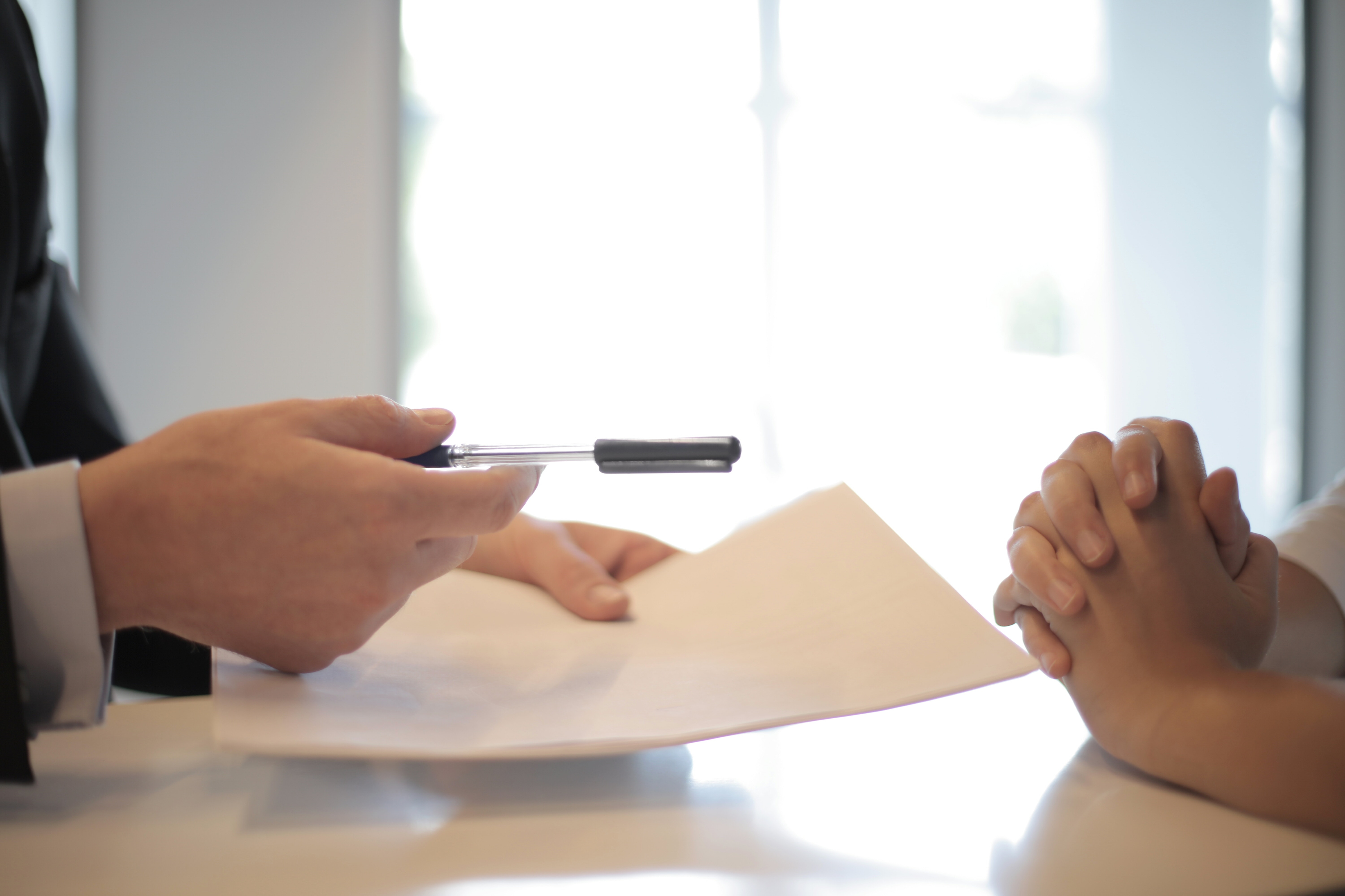 a person in a suit handing a customer a paper and pen to sign a document