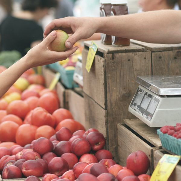 a cashier handing someone a fruit at a farmer's market