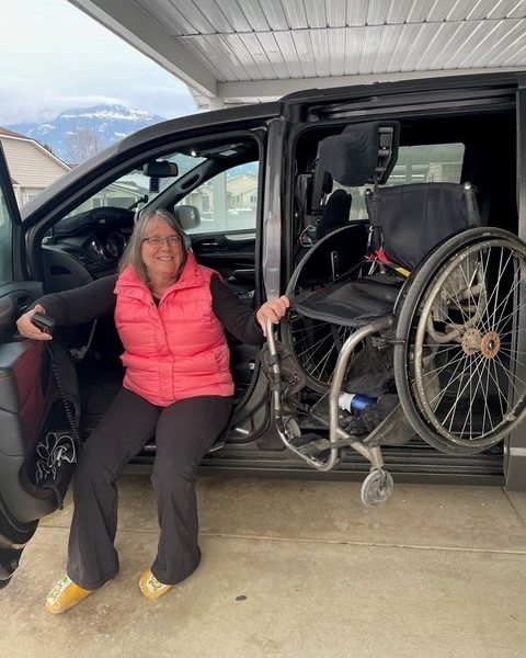 Joan sitting in her adapted van with the door open, with her wheelchair being loaded into her van
