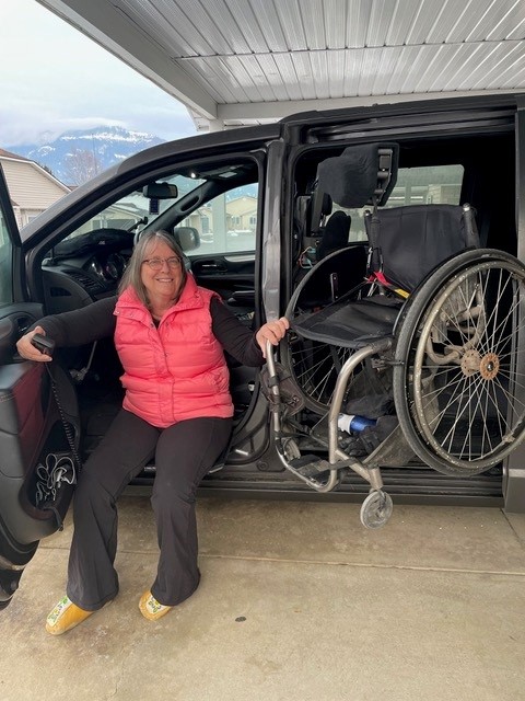 Joan sitting in her adapted van with the door open, with her wheelchair being loaded into her van